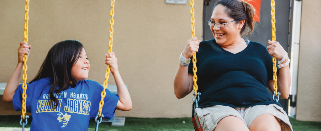 mother and young daughter sitting and swinging