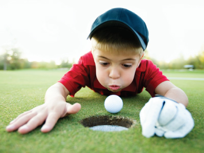 young boy playing golf close to the hole blowing against ball close to cup