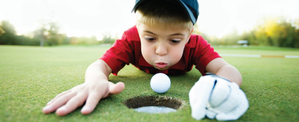 Photo-SFTH young boy playing golf close to the hole blowing against ball close to cup